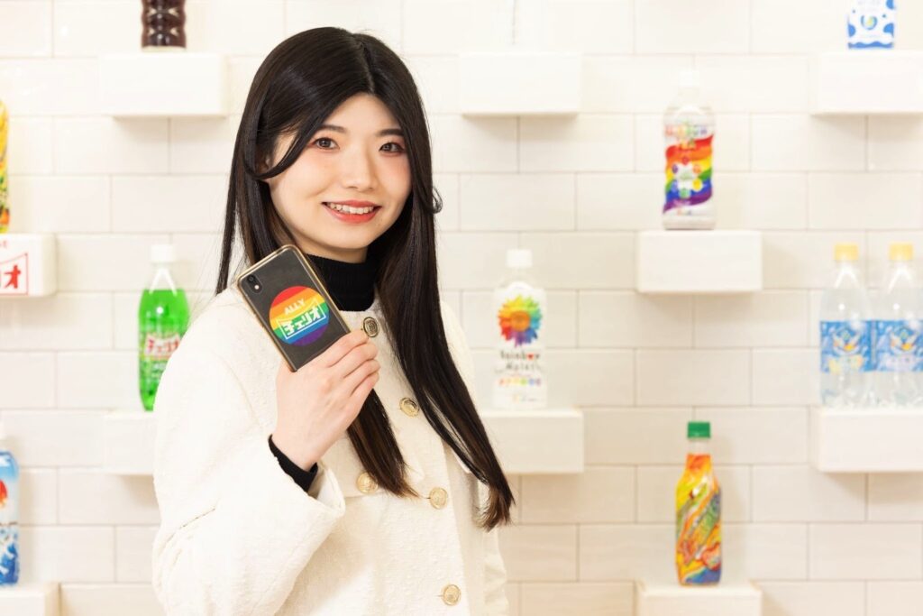 アライシールを貼ったスマートフォンを掲げるマーケティング部の西尾友希さん